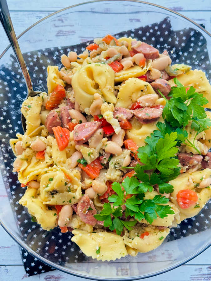 a big bowl of tortellini pasta salad garnished with flat leaf parsley