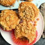 three coffee cake muffins on a plate and one has a bite taken out of it