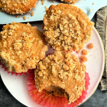 three coffee cake muffins on a plate and one has a bite taken out of it