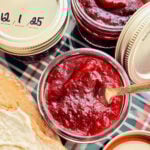 an open jar of cranberry jam ready to spread on a slice of buttered bread