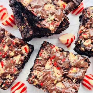 five squares of peppermint brownies displayed with unwrapped candy cane kisses