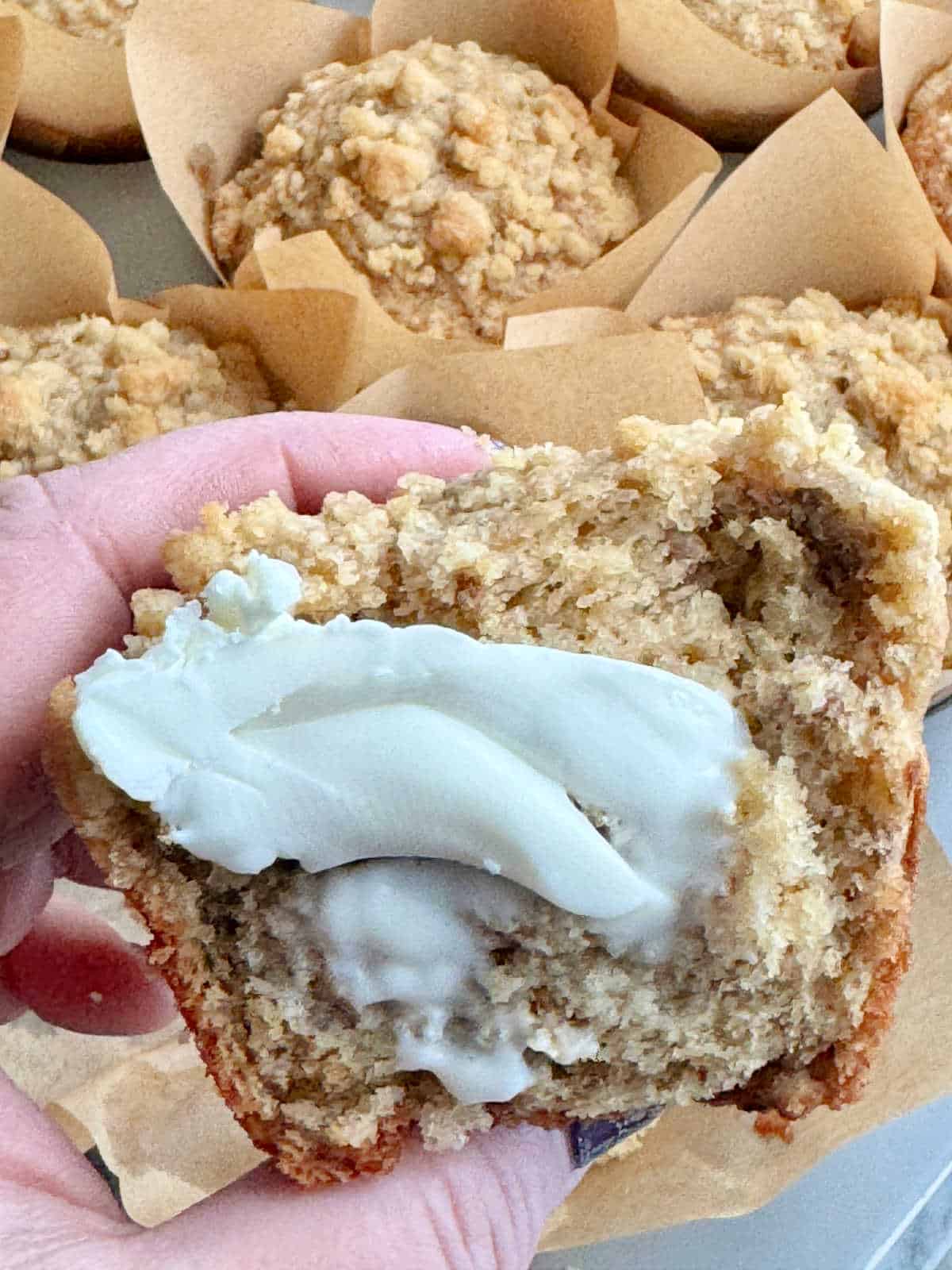 holding a buttered half of bakery style banana bread muffin