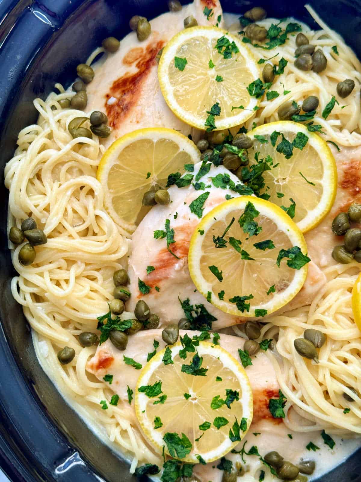 angel hair pasta topped with crock pot chicken piccata and garnished with lemon slices ready to serve