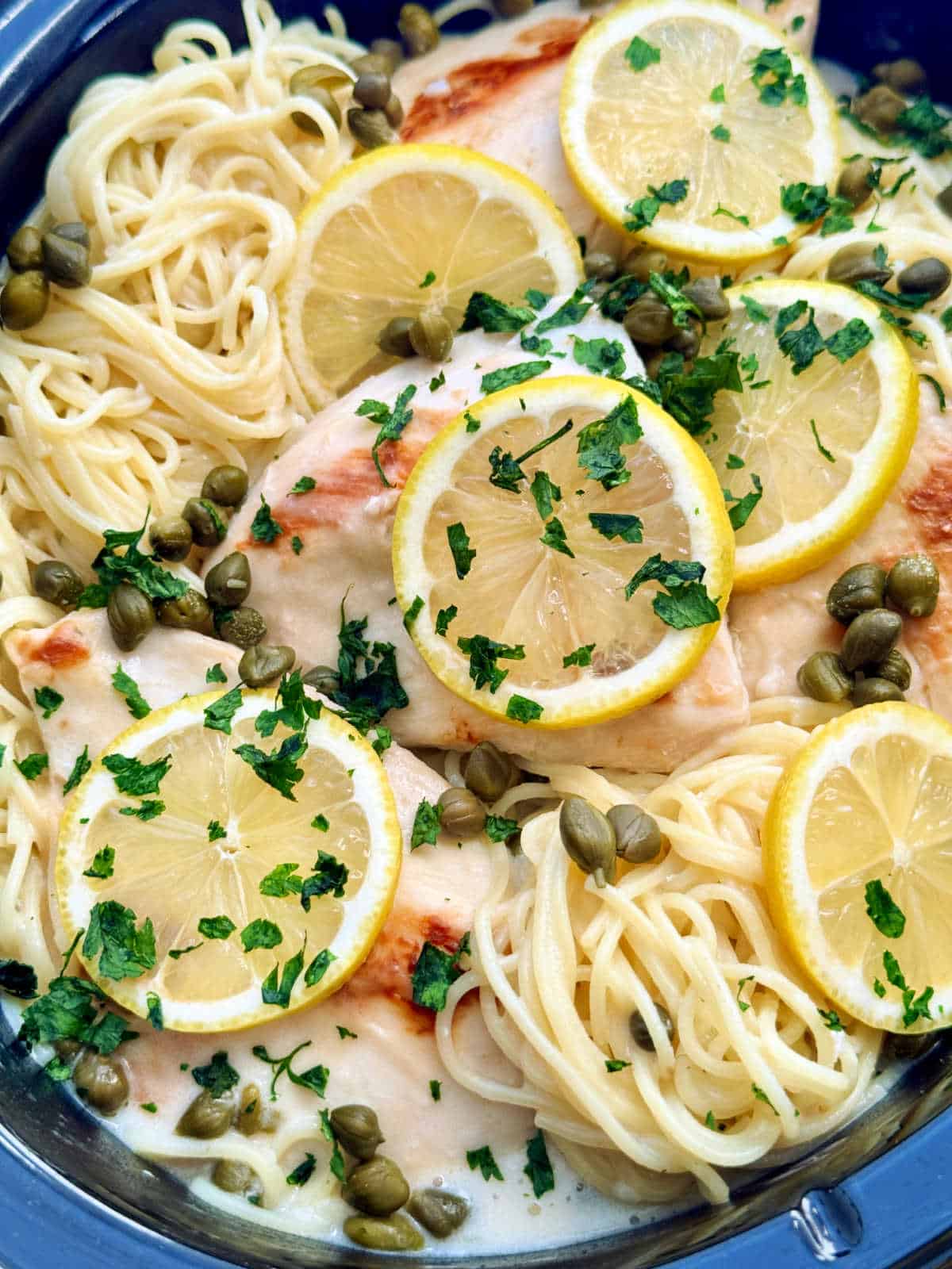 a closer up picture of the chicken piccata and angel hair pasta in the slow cooker insert