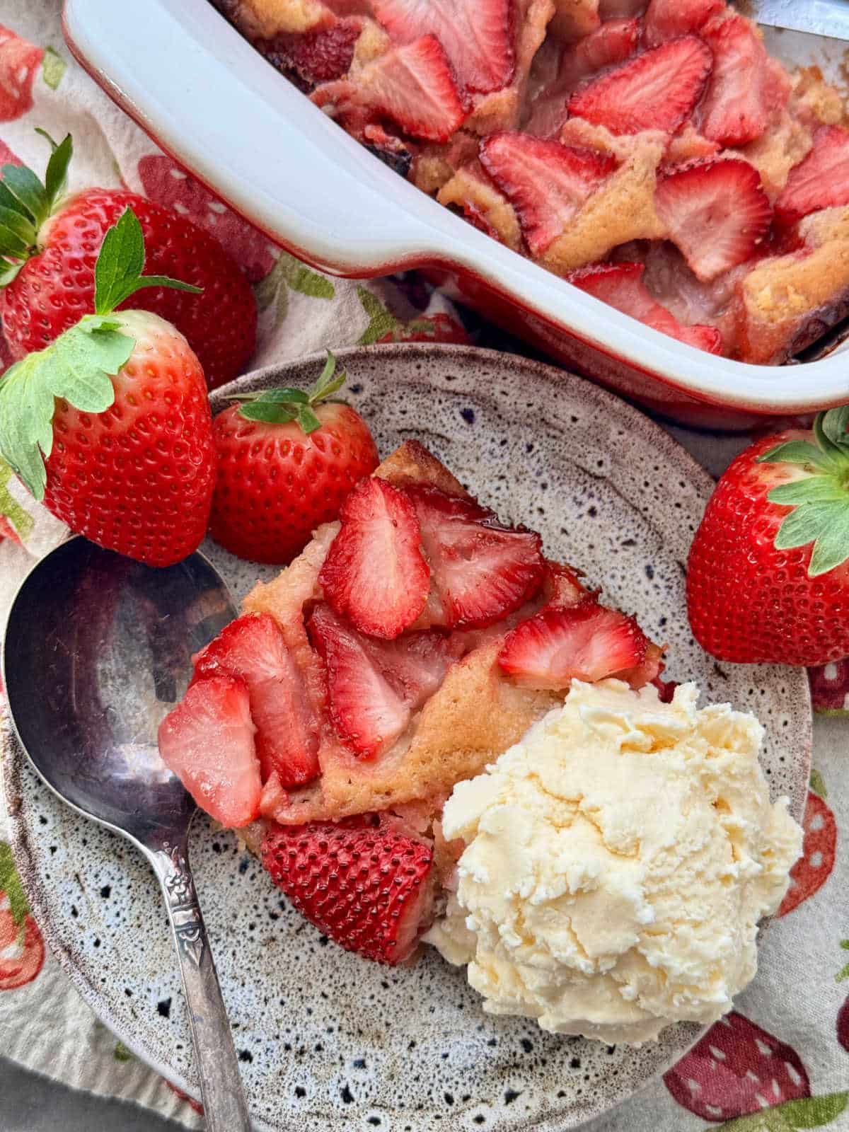 a slice of strawberry cobbler plated with a scoop of vanilla ice cream and garnished with fresh berries