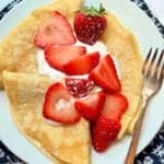 three plated crepes topped with fresh strawberries and whipped cream