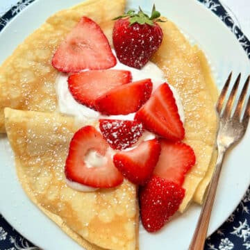 three plated crepes topped with fresh strawberries and whipped cream