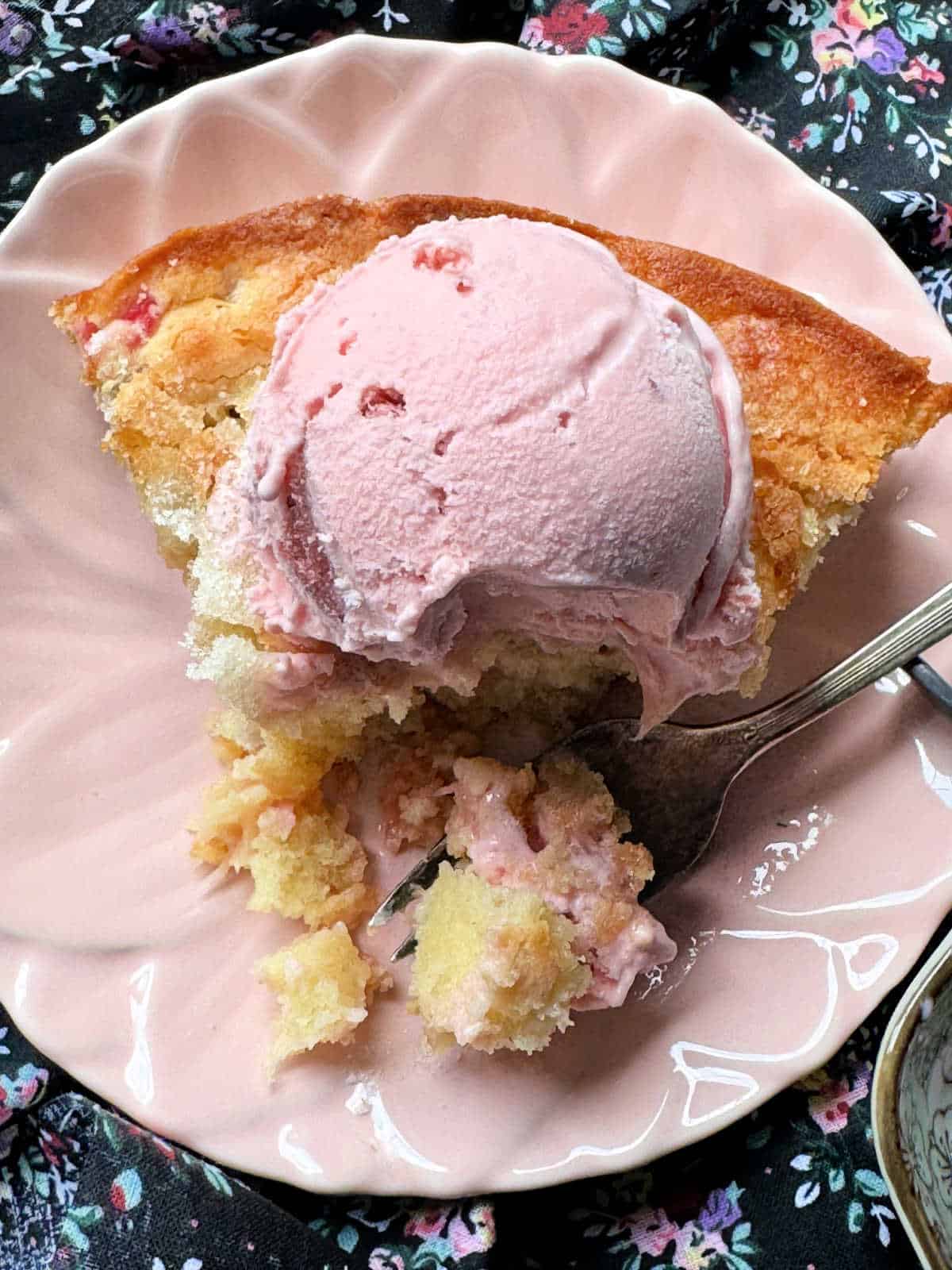 a slice of rhubarb cake topped with strawberry ice cream and a bite taken out of it