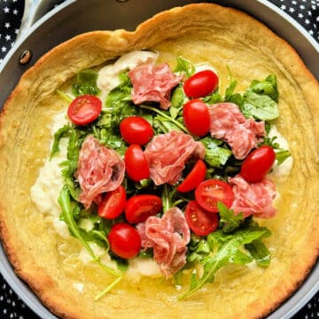 savory dutch baby pancake topped with arugula, burrata cheese, salami and tomatoes