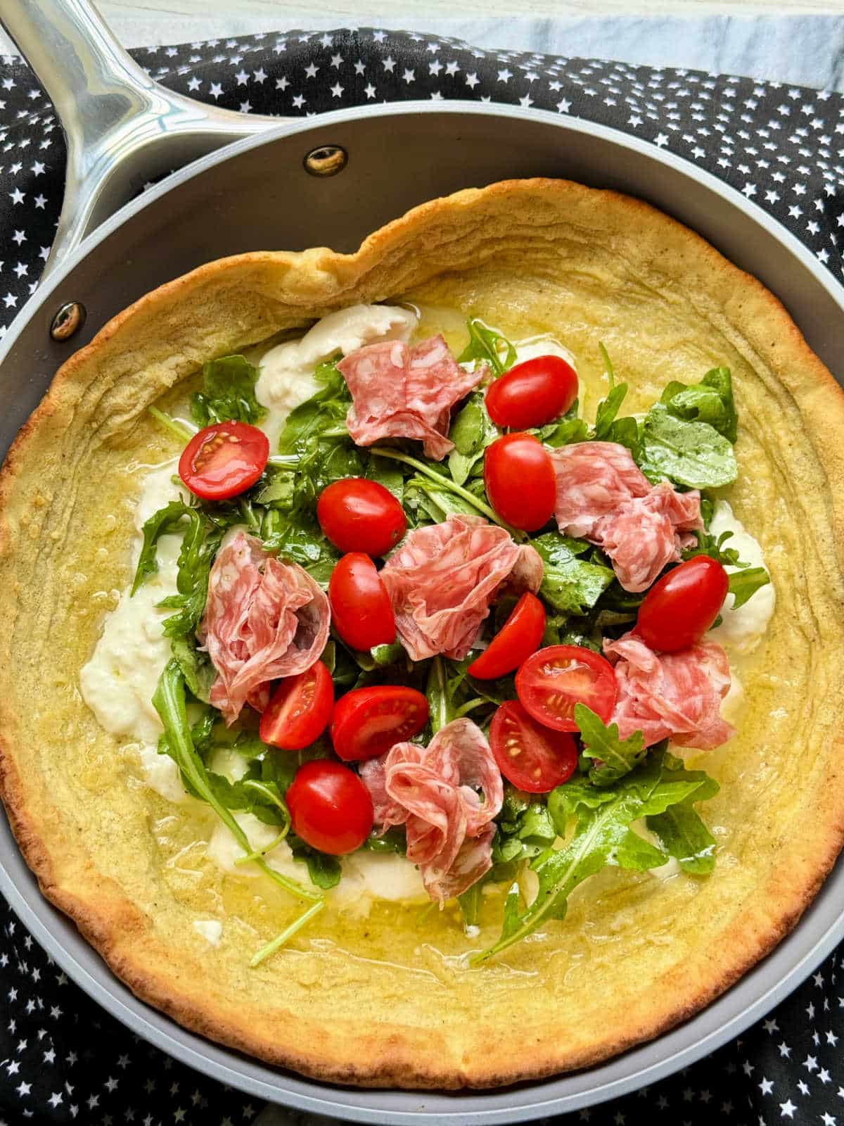 savory dutch baby in skillet topped with arugula, burrata cheese, salami and tomatoes