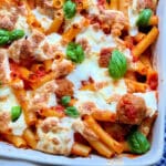 baked dish of ziti pasta with meatballs topped with burrata cheese and garnished with fresh basil