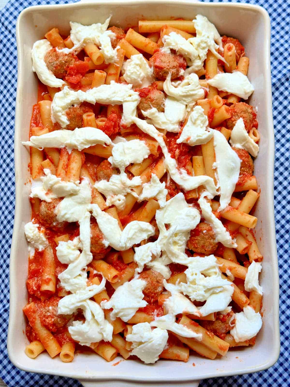 a dish of ziti with meatballs and topped with burrata cheese before being baked