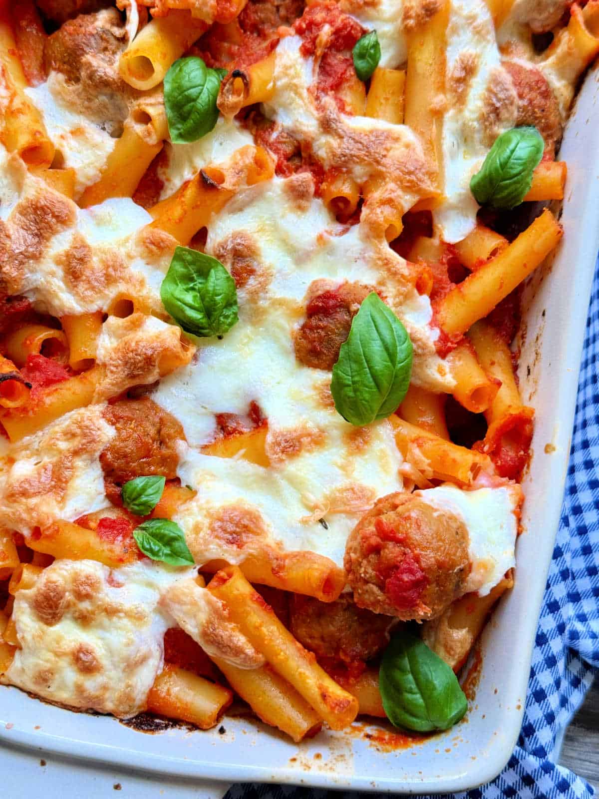 an overhead view of baked ziti with meatballs garnished with fresh basil leaves