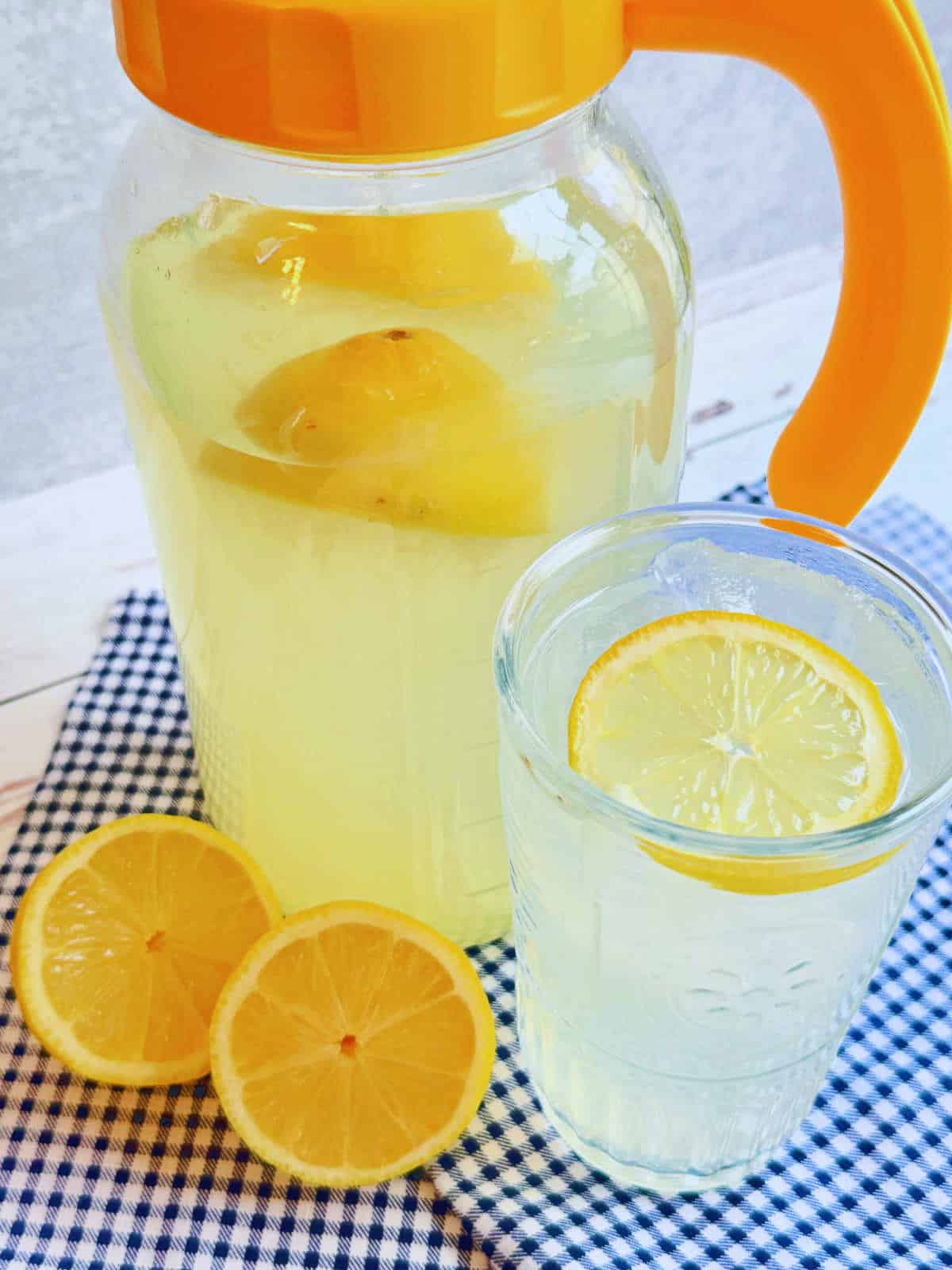 a pitcher of homemade lemonade and a glass filled with ice and lemonade and garnished with a lemon slice