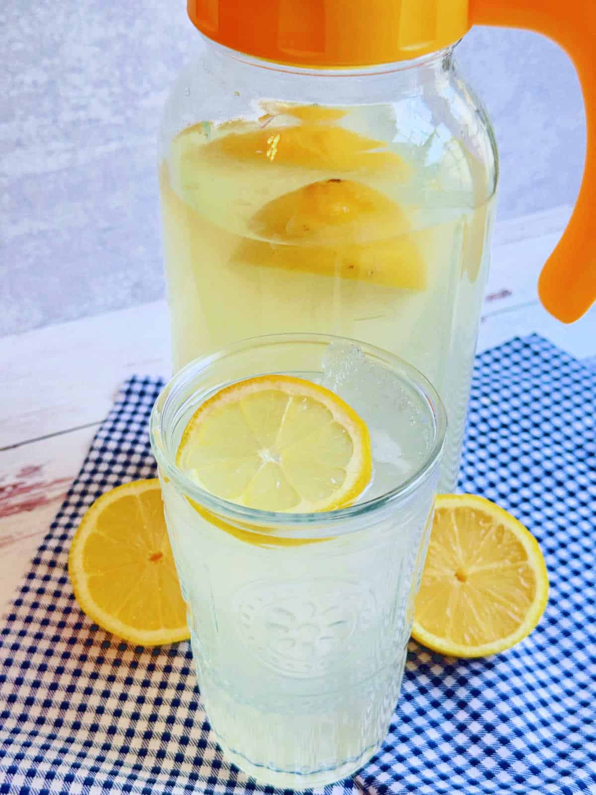 a cold glass of lemonade over ice in front of the pitcher it was poured from 