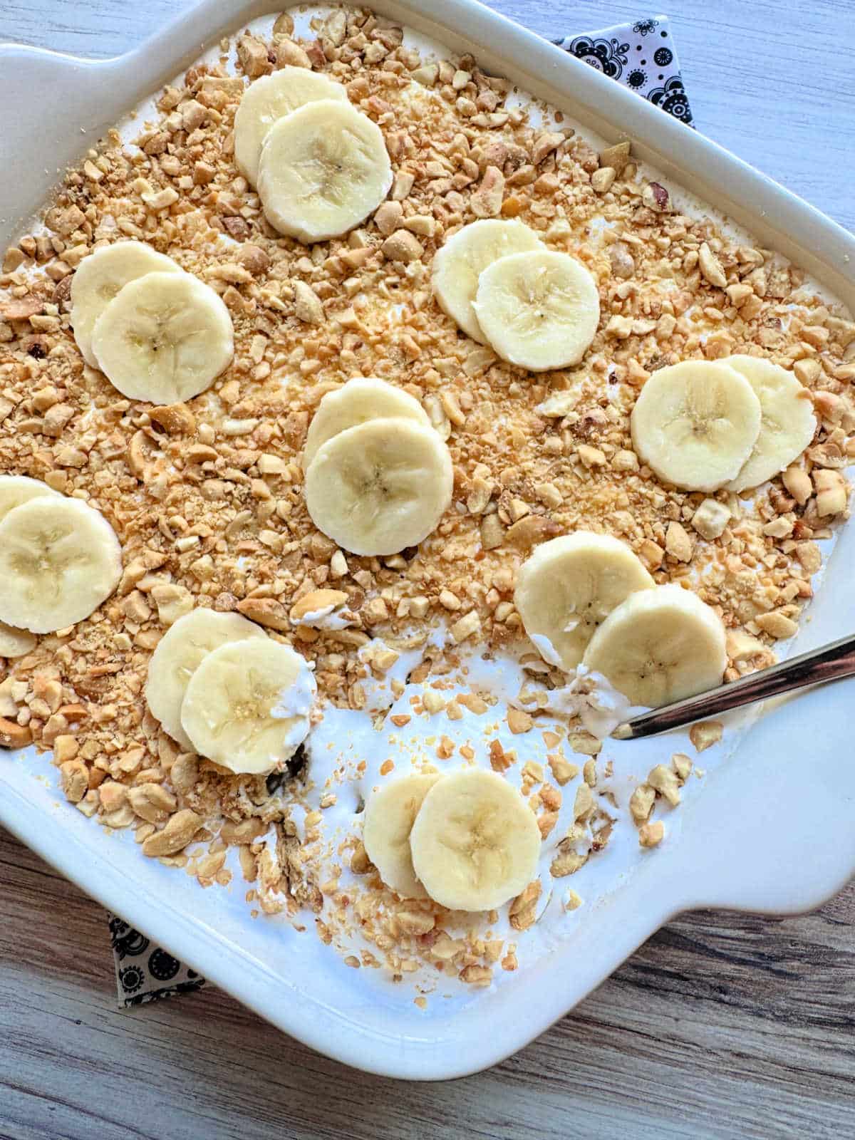 a dish of banana pudding topped with crushed peanuts and sliced bananas