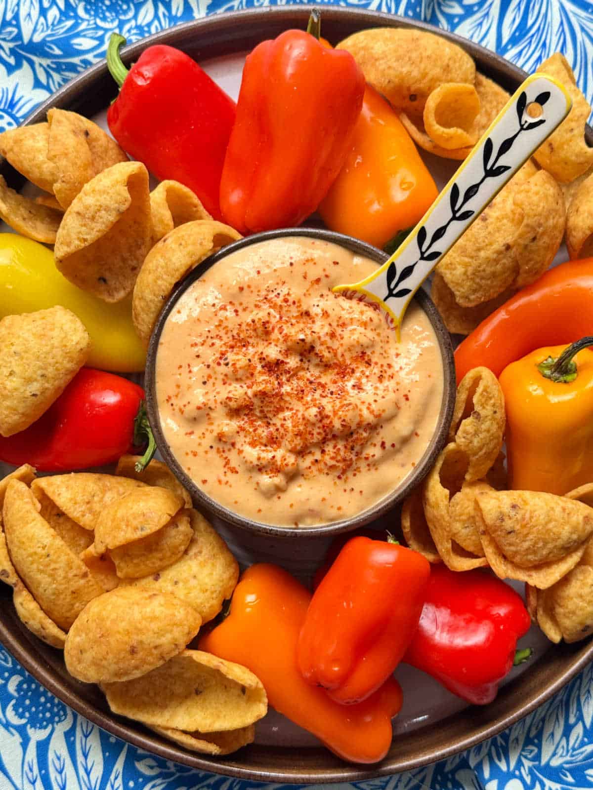 a bowl of corn dip set on a platter with mini peppers and Frito scoops