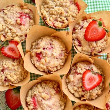 a display of fresh strawberry muffins set on a green and white checked cloth and garnished with fresh strawberries sliced in half
