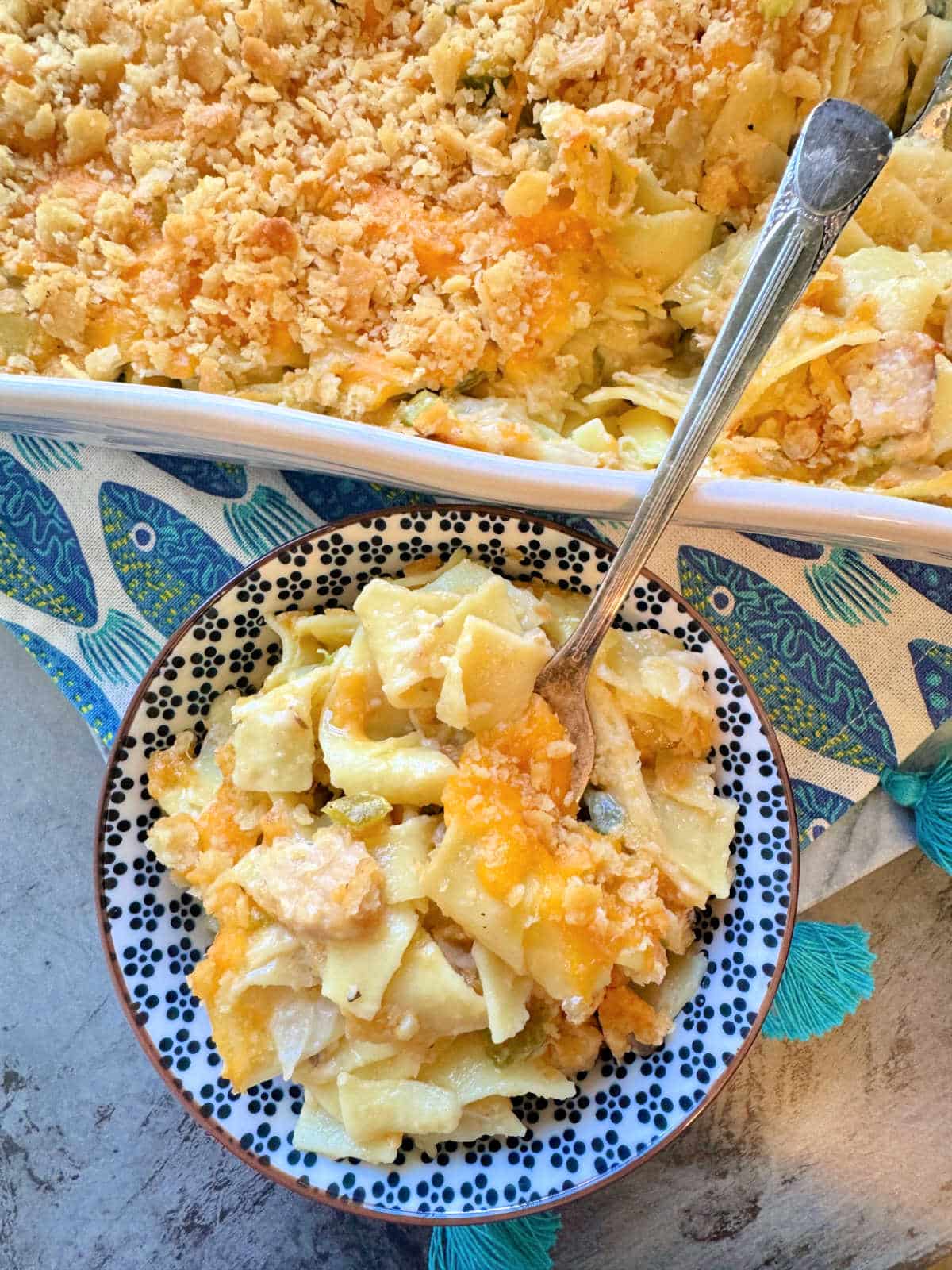 a small serving bowl filled with casserole in front of the baking dish of tuna noodle casserole