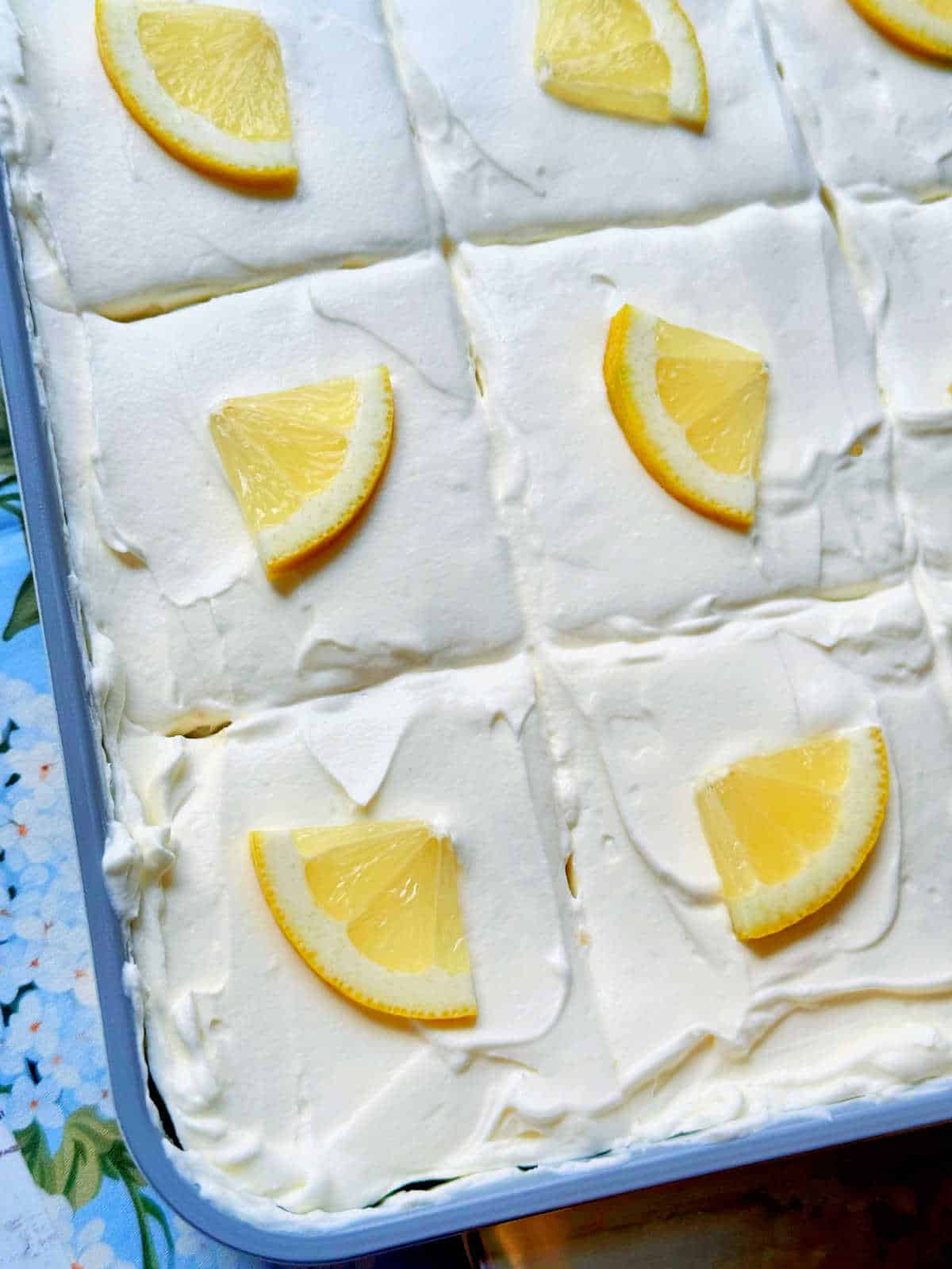 showing sliced lemon poke cake garnished with lemon slices ready to serve from the pan