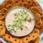 a bowl of pickle dip garnished with more chopped dill pickles and surrounded by pretzel crisps for dipping