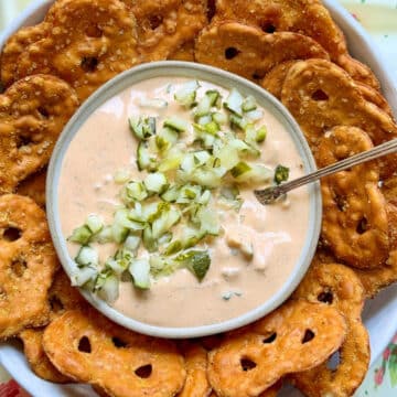 a bowl of pickle dip garnished with more chopped dill pickles and surrounded by pretzel crisps for dipping
