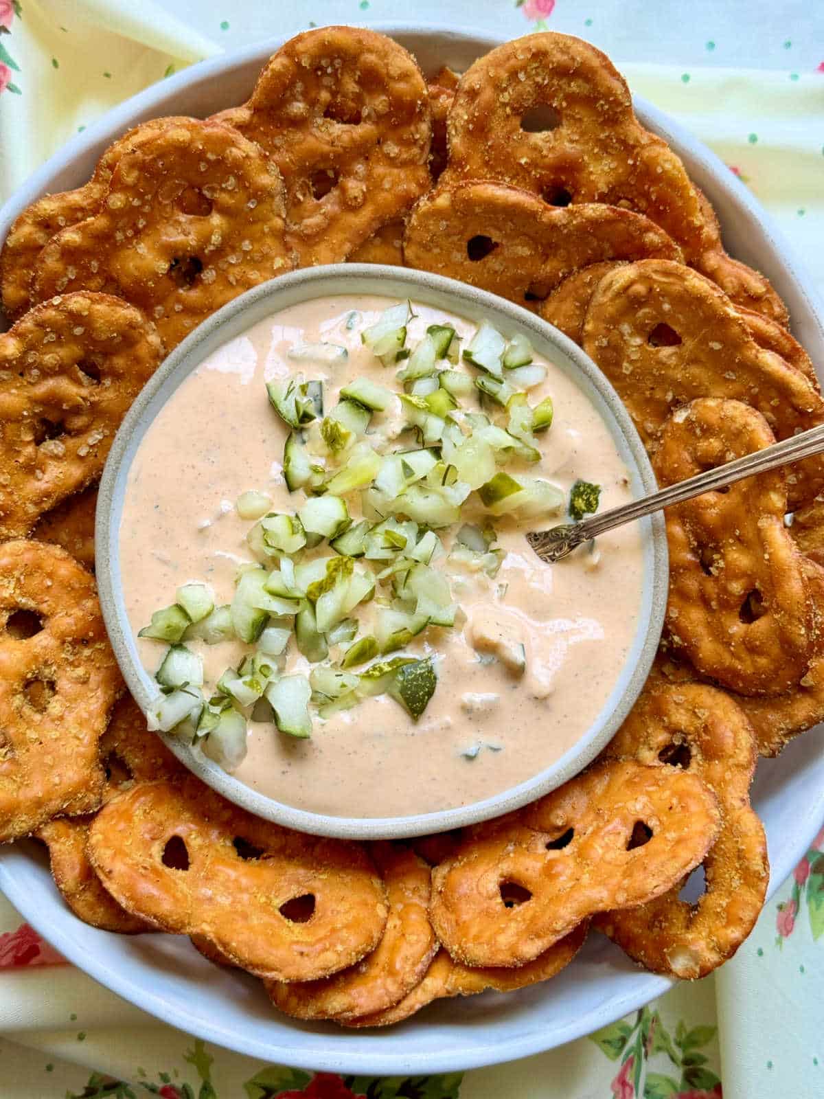 a bowl of pickle dip garnished with chopped pickles and surrounded by pretzel crisps for dipping