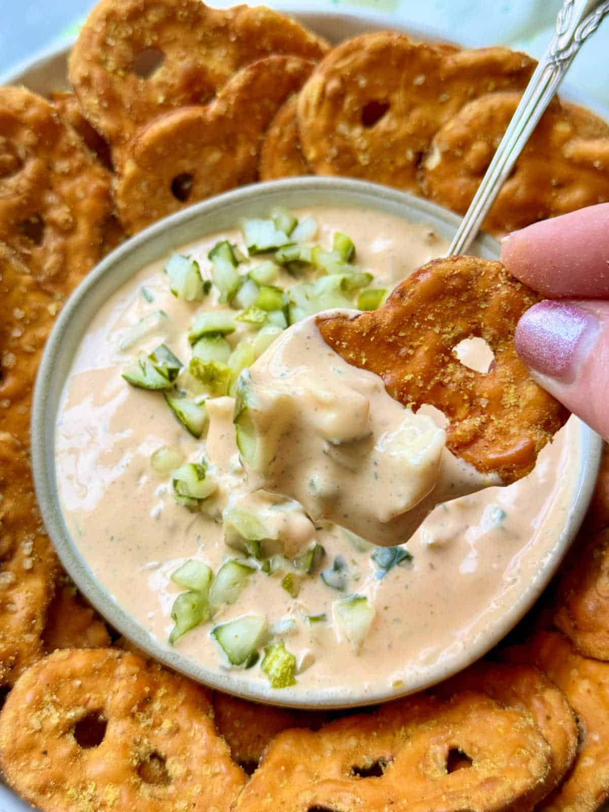 dipping a honey mustard pretzel crisp into a bowl of dill pickle dip
