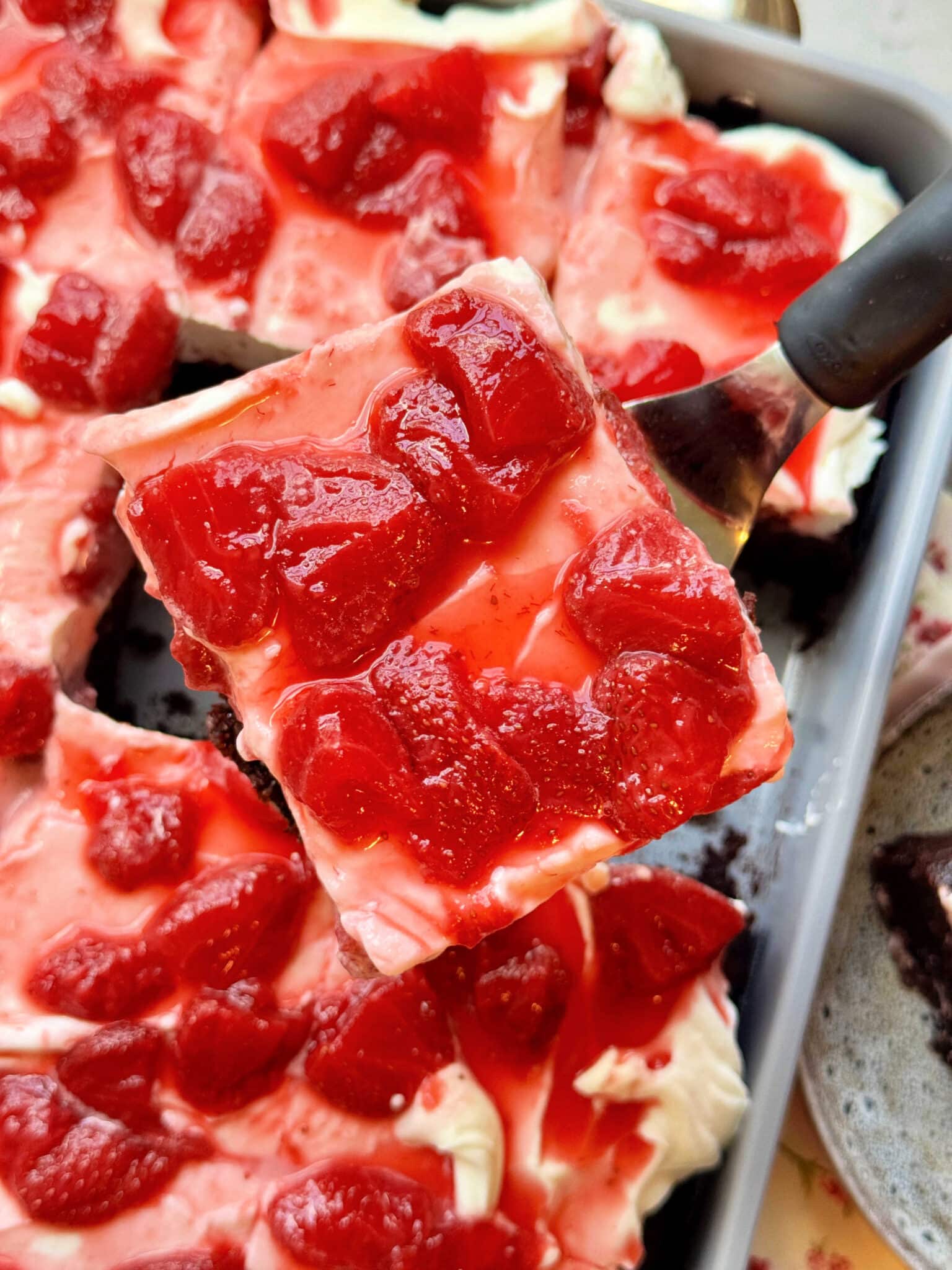 using a small spatula to lift a slice of chocolate strawberry cake from its pan