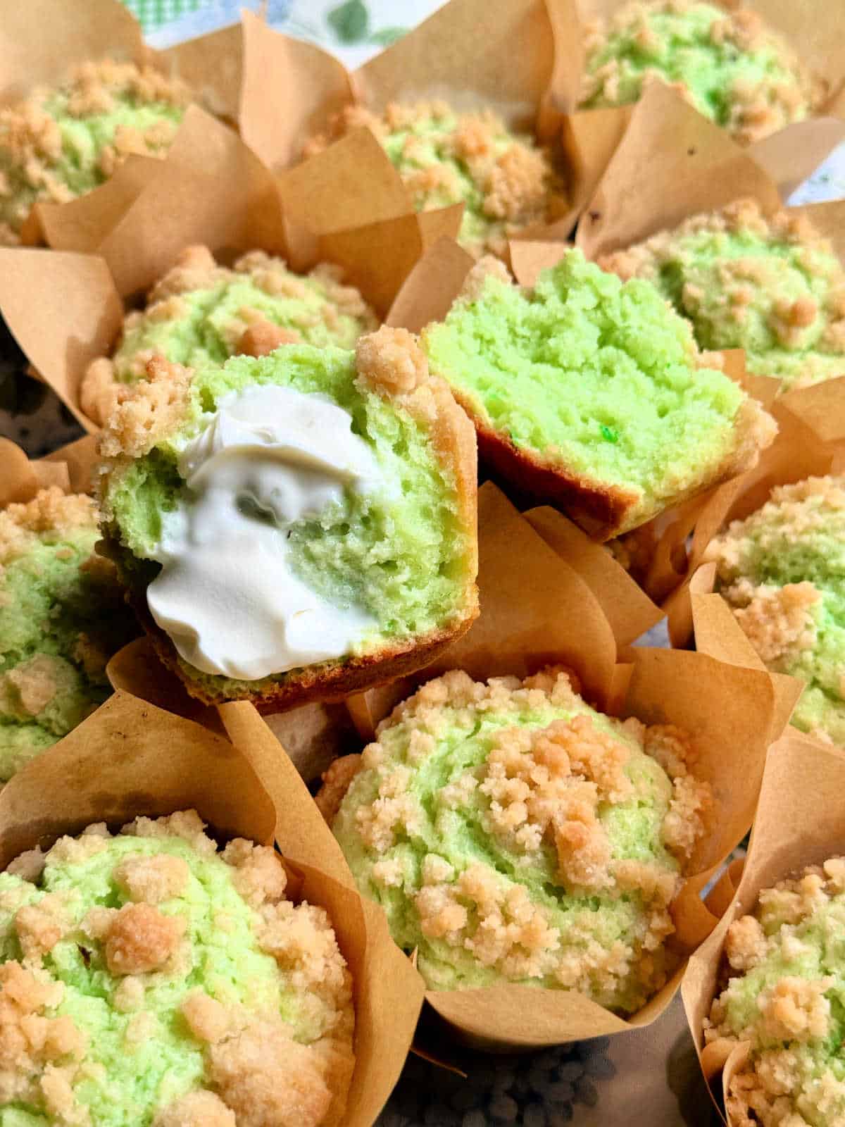 a halved muffin spread with butter resting atop the rest of the dozen pistachio muffins