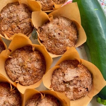 a dozen zucchini muffins displayed alongside a fresh zucchini