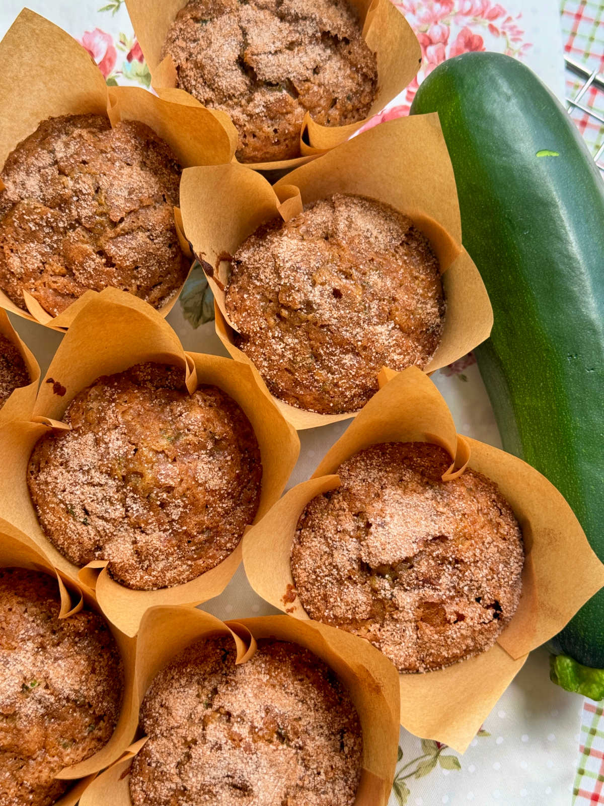 freshly baked zucchini muffins arranged on a floral background next to a whole zucchini
