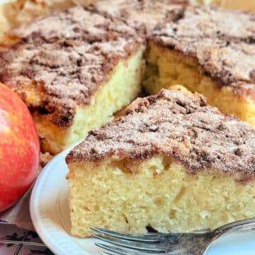 plated slice of apple cake in front of the whole sliced fresh apple cake