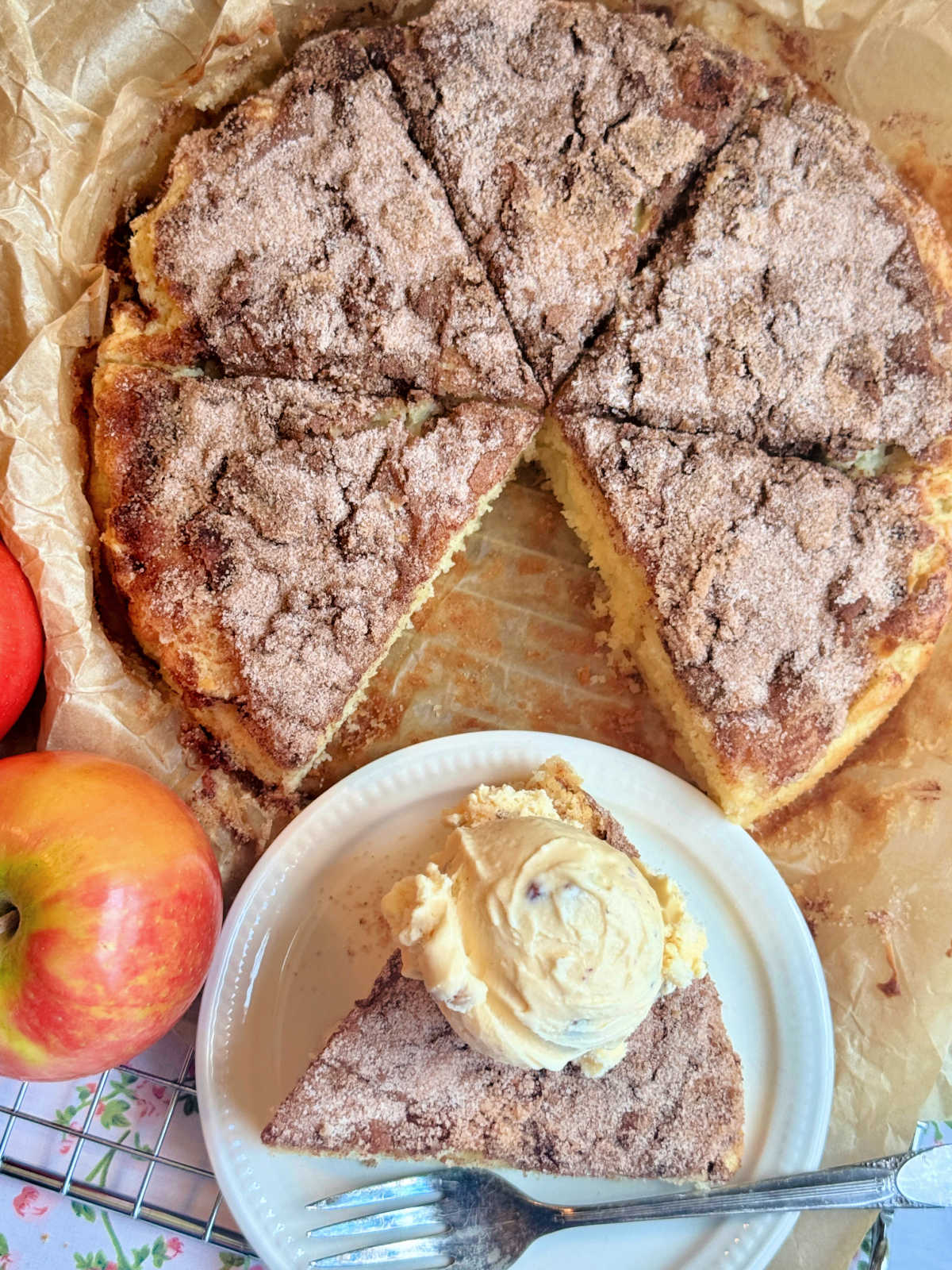 a plated slice of apple cake topped with butter pecan ice cream and setting in front of the whole cake