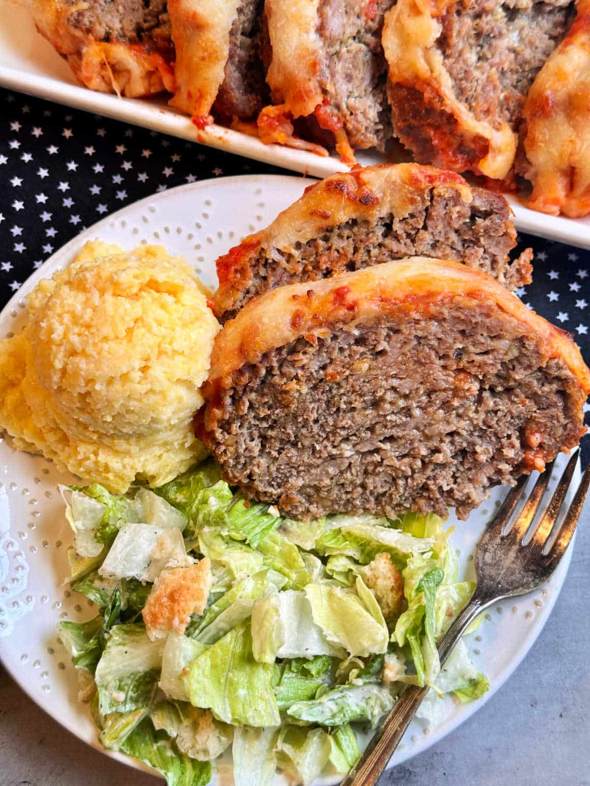 two slices of Italian meatloaf plated with polenta and Caesar salad